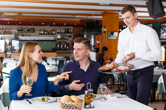 Waiter serving tasty dishes to couple