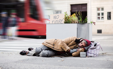 Homeless beggar man lying on the ground outdoors in city asking for money donation.