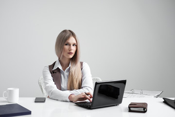 Blonde girl in a business suit works on a computer in a white bright office.