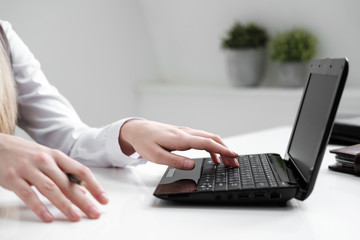 Close-up, girl's hands on the background of the white table, typing on a laptop.