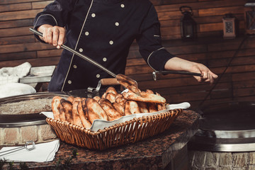 Baker making turkish pita bread in tandoor (clay oven). Baking process. Many fresh hot bread in the basket