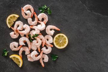 Fresh shrimps or frozen prawn with lemon on slate stone background. Seafood, top view, flat lay, copy space