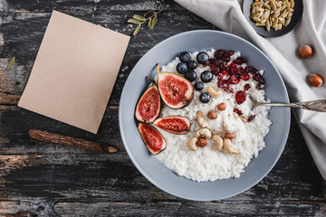 Rice coconut porridge with figs, berries, nuts, dried apricots and sheet of paper on rustic wooden background. Healthy breakfast ingredients. Clean eating, vegan food concept. Top view