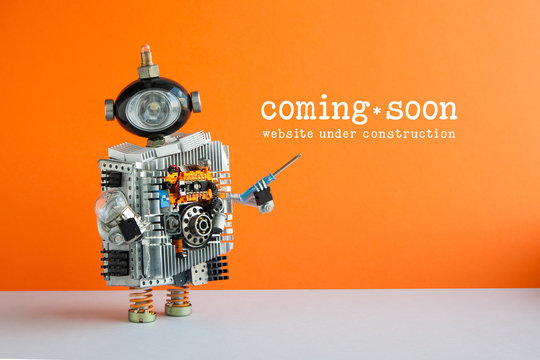 Web Site Under Construction Coming Soon Page. Toy Robot With Screwdriver And Light Bulb. Orange Wall Gray Floor Background.