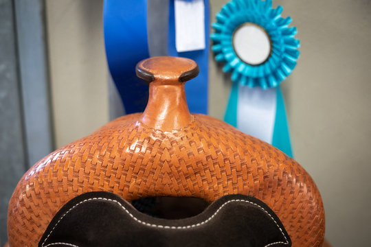 Close up on the horn of a leather horse riding saddle, with blue ribbons in the background