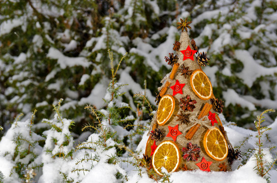 Необычная новогодняя ель, выполненная в стиле «арт-деко» украшенная сушеными апельсинами, сосновыми шишками и корицей на фоне заснеженной хвои.