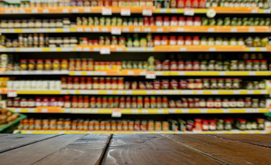 Supermarket, grocery department. Defocused, blurred image. In the foreground is the top of a wooden table, counter.