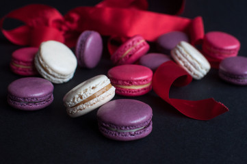 Obraz na płótnie Canvas macaroon on black background with red ribbon, colorful almond cookies, pastel colors.