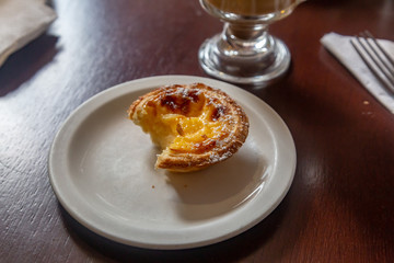 A Portuguese custard tart on a plate in a coffee shop, with a bite taken out of it