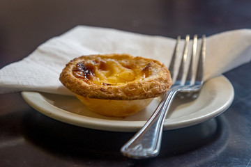 A Portuguese custard tart on a plate in a coffee shop, ready to be eaten