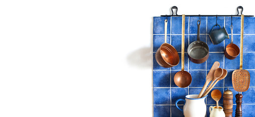 Kitchen interior with vintage copper utensils. old style cookware kitchenware set. Pots, kitchen spoon, skimmer hanging on blue tile wall. Copy space, white background