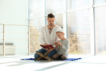 Muslim man and his son reading Koran together indoors © New Africa