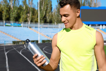 Sporty man with bottle of water at stadium on sunny day