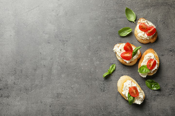 Pieces of baguette with tasty cream cheese and tomatoes on gray table, flat lay. Space for text