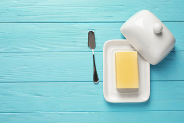 Dish with fresh butter and knife on wooden background, top view. Space for text