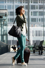 Obraz premium Happy travel woman walking at station with suitcase and talking on cellphone