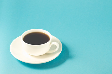 espresso cup on a blue background/white cup with a saucer full of black coffee on a blue background, selective focus