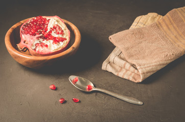 cut into pieces red garnet in a wooden bowl on the table/parts of pomegranate in a wooden bowl and a spoon against a dark background