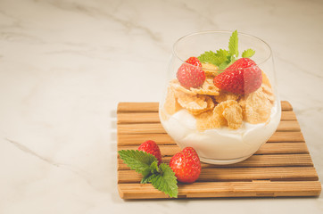 Glass of tasty strawberry dessert/Smoothies with corn flakes decorated mint and strawberry on a marble background with copyspace