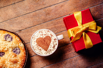 Christmas pie and cup of coffee with heart shape with gift boxes around on wooden table. Hight angle point of view