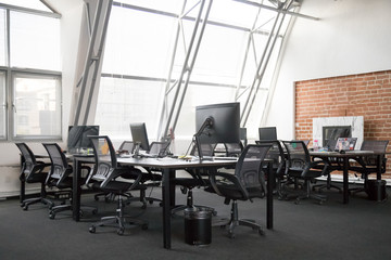 Modern view of empty office space interior, open plan office concept, trendy loft workspace with big windows, lot of office equipment, computers, monitors, natural light, creativity, without people