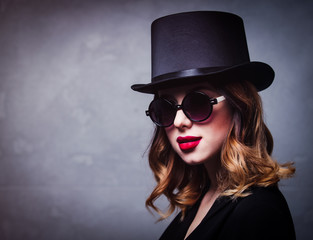 Style and mystique redhead girl in top hat and sunglasses on grey background