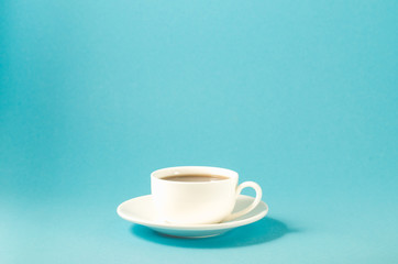 white cup with black coffee on a blue background/white cup with a saucer full of black coffee on a blue background