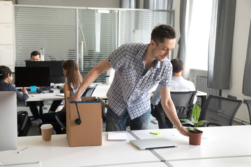 Happy young man, intern unpack cardboard box with belongings at workplace, starting work in new...