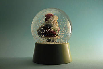 Santa Claus carrying his bag in a snowstorm globe isolated on blue background.