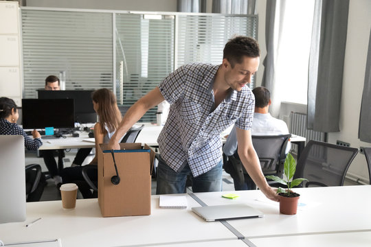 Happy young man, intern unpack cardboard box with belongings at workplace, starting work in new company, first day of job, prepare to beginning of working day, newly hired office worker, newcomer