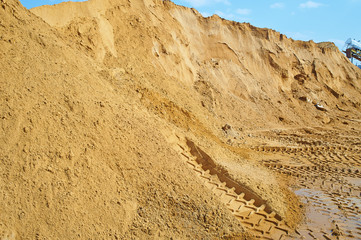 A mountain of sand in a career with track of an excavator or tractor