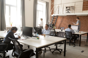 Serious diversity team of focused employees working online project in modern office space, using computers, teamwork, routine work day, busy office workers at workplace, white mock up monitor