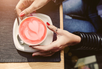 Woman's hands holding cup of cappuccino on wooden table. Living Coral colored picture. Beverage concept of color of the year 2019. Top view, flat lay, copyspace for text