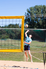 Beach volleyball player in action at sunny day under blue sky. volleyball net in the foreground, vertical.