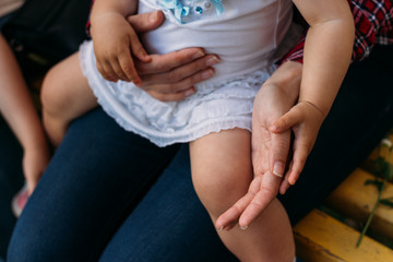 a little girl sits in the arms of a girl, she is hugged behind her back and holding hands. extends a hand to take a small hand