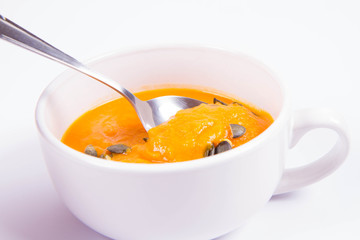 Pumpkin soup decorated with pumpkin seeds being eaten with a spoon on a white background