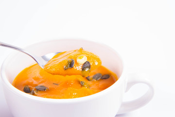 Pumpkin soup decorated with pumpkin seeds in a bowl on a white background