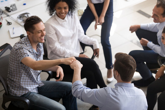 Male smiling colleagues fist bumping, congratulating, celebrating good teamwork results at company meeting, training, happy employees sharing success, involved in team building activity, top view