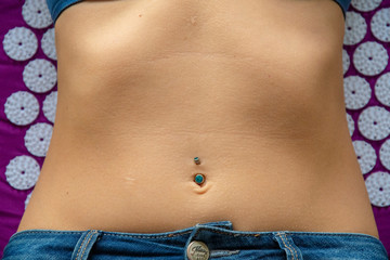 naked belly of a young woman with piercing and jeans lying on her back