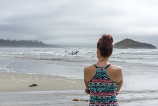 Young attractive girl standing alone watching the waves and surfers in the distance on Long Beach in Pacific Rim National Park Reserve on the west coast of Vancouver island