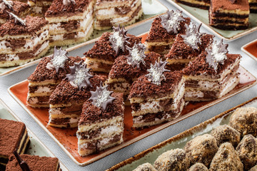 Cakes tiramisu with chocolate, cocoa and candies on holiday background. Delicious dessert and candy bar