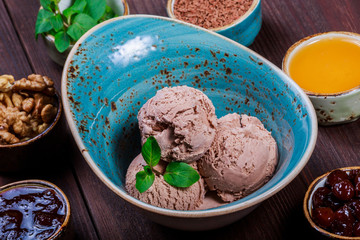 Chocolate ice cream scoops in bowl with mint leaves on wooden background