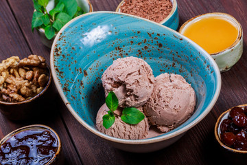 Chocolate ice cream scoops in bowl with mint leaves on wooden background