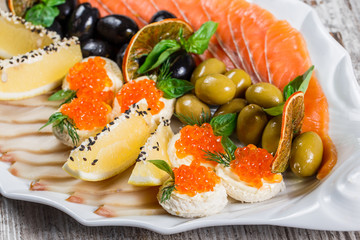 Seafood platter with salmon slice, quail eggs with red caviar, slices fish fillet, decorated with olives and lemon in plate over rustic background. Mediterranean appetizers