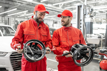 Portrait of a two auto mechanics in red uniform standing with disks for wheel alignment at the car service