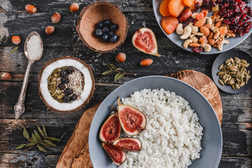 Rice coconut porridge with figs, berries, nuts, dried apricots and coconut milk in plate on rustic wooden background. Healthy breakfast ingredients. Clean eating, vegan food concept, close up