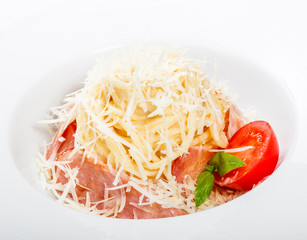 Fettuccine pasta with meat, ham, parmesan cheese, basil and tomato on plate on light wooden background, Italian cuisine. Ingredients on table