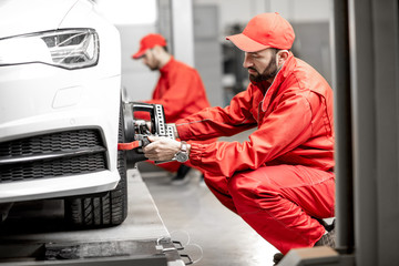 Two auto mechanics in red uniform fixing disk for wheel alignment on a luxury car at the car service