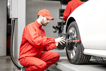 Handsome auto mechanic in red uniform fixing disk for wheel alignment at the car service