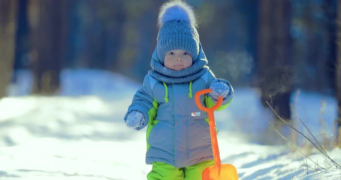 Kid walks through the winter forest. Holds a spade in his hands. Smiles Close-up